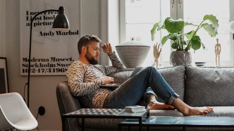Eine Person sitzt mit einem Laptop auf den Knien auf einem Sofa.