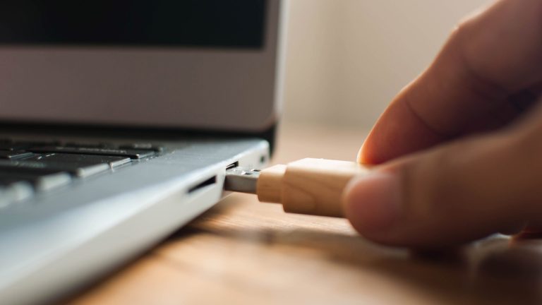 Eine Hand steckt einen USB-Stick in den Anschluß eines Laptops.