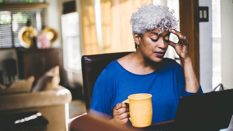 Eine Person sitzt mit einer Tasse in der rechten Hand vor einem Laptop.