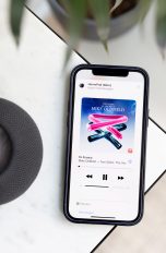 HomePod Apple Music Ein schwarzer HomePod mini steht auf einem Marmortisch. Neben dem Lautsprecher liegt ein iPhone, auf dem Apple Music geöffnet ist.