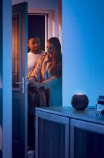 Philips Hue Apple HomeKit Zwei Personen betreten eine Wohnung, in der auf einer Anrichte ein HomePod mini in Schwarz steht.