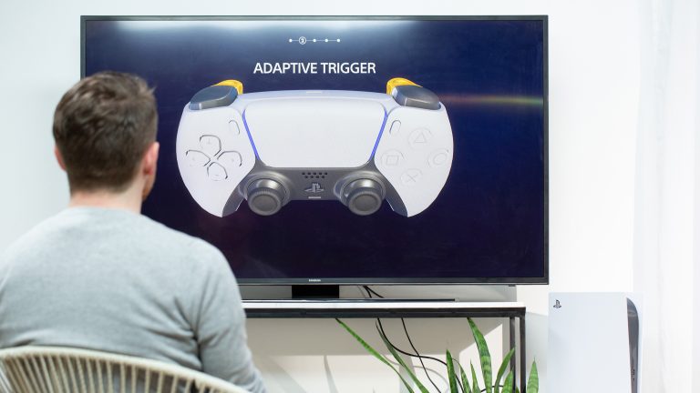 Eine Person sitzt vor einem Fernseher und schaut sich die Erklärung zu den adaptiven Triggern im DualSense an.