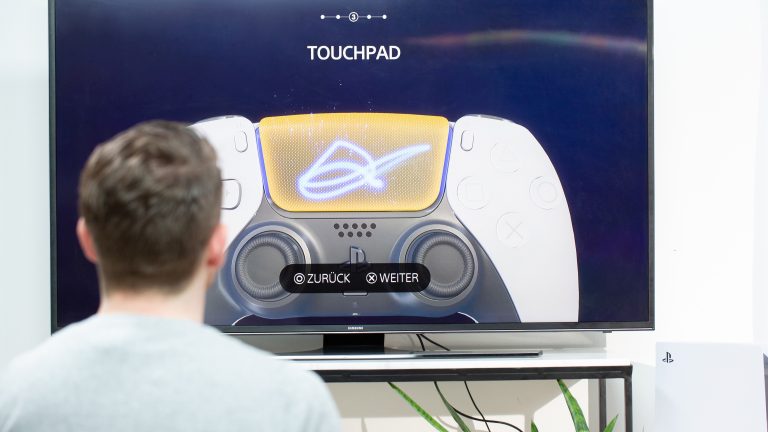 Eine Person sitzt vor einem Fernseher und schaut sich den Erklärfilm zum Touchpad im DualSense-Controller an.