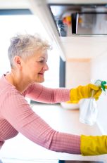 Eine Person putzt die Fliesen ihrer Küchenzeile. Hierbei benutzt sie gelbe Handschuhe und eine Sprühflasche.