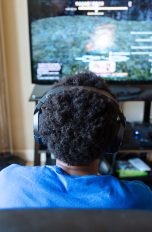 Grafikkarte defekt Eine Person sitzt vor einem Fernseher, auf dem gerade ein Computerspiel läuft. Links davon steht ein aufgeklappter Laptop.