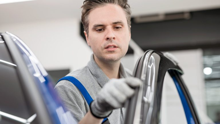 Eine Person in einem Blaumann f&auml;hrt mit dem Zeigefinger die Gummidichtung einer ge&ouml;ffneten Autot&uuml;r ab.