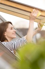 Eine Person reibt mit einem gelben Schwamm an den R&auml;ndern eines ge&ouml;ffneten Dachfensters entlang.