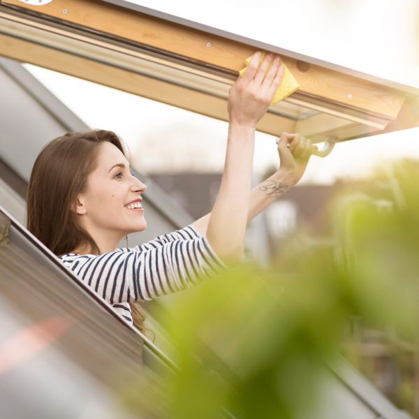 Eine Person reibt mit einem gelben Schwamm an den R&auml;ndern eines ge&ouml;ffneten Dachfensters entlang.