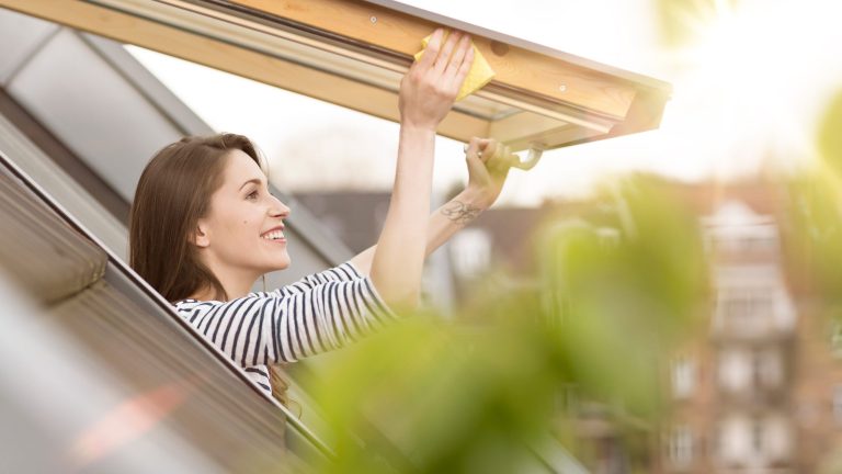 Eine Person reibt mit einem gelben Schwamm an den R&auml;ndern eines ge&ouml;ffneten Dachfensters entlang.