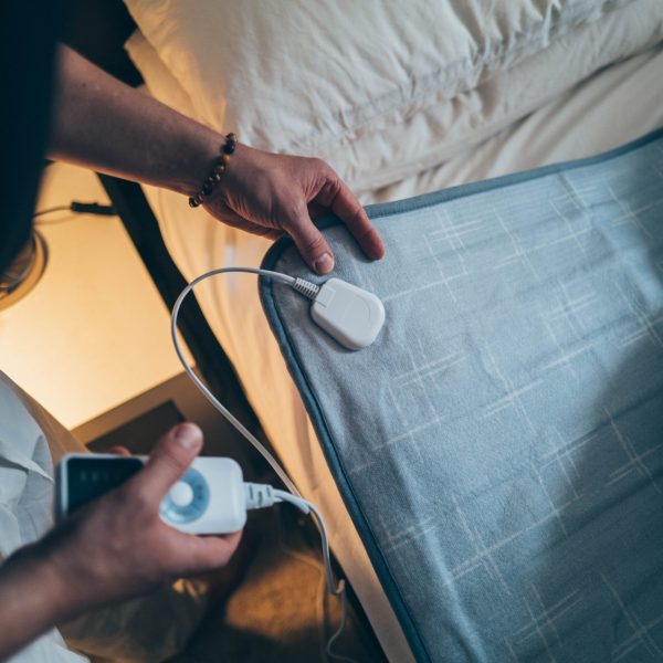 Eine Person stellt die Temperatur einer Heizdecke ein, die ausgebreitet auf einer Matratze liegt.