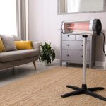 Eine Infrarotheizung auf einem Standfuß steht auf einem Teppich mittig in einem Raum.