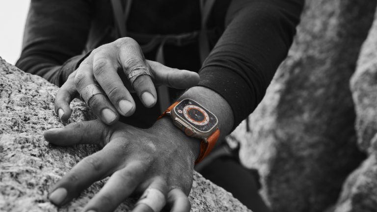 Die Apple Watch Ultra am Handgelenk einer Person. Die Uhr ist dabei farbig in einem sonst schwarz-weißen Foto.
