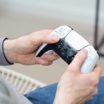 Eine Person h&auml;lt einen wei&szlig;en DualSense-Controller in der Hand.