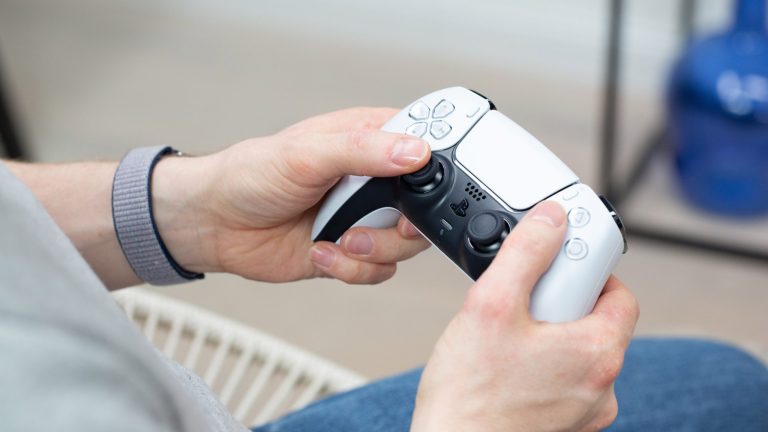 Eine Person hält einen weißen DualSense-Controller in der Hand.