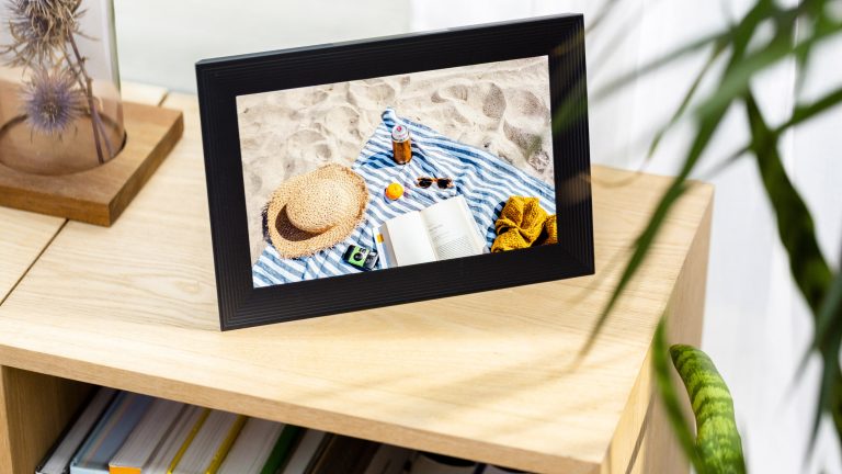 Ein schwarzer Bilderrahmen mit einem Strandfoto ziert ein Regal aus hellem Holz. aura-bilderrahmen-0044
