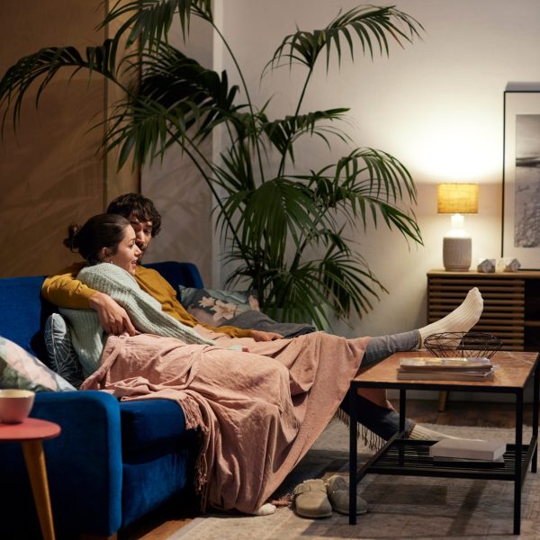 Zwei Personen sitzen auf einem Sofa unter einer Decke und schauen gemeinsam etwas an.