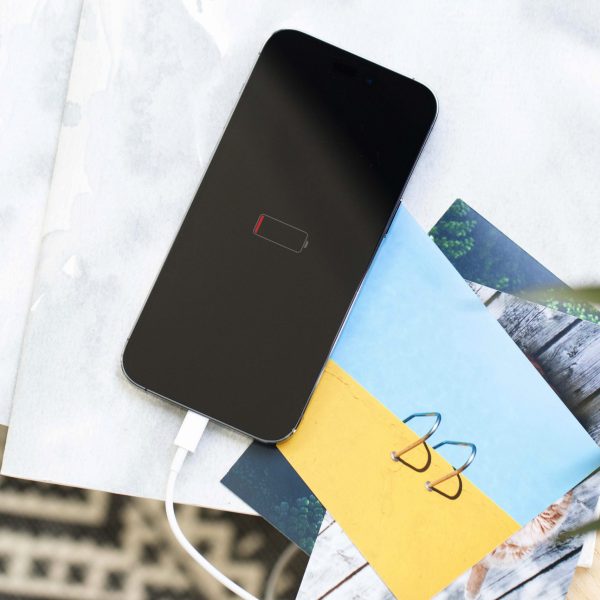 Ein leeres iPhone liegt auf einigen Zetteln und Postkarten. Auf dem Display ist eine leere Batterie zu sehen.