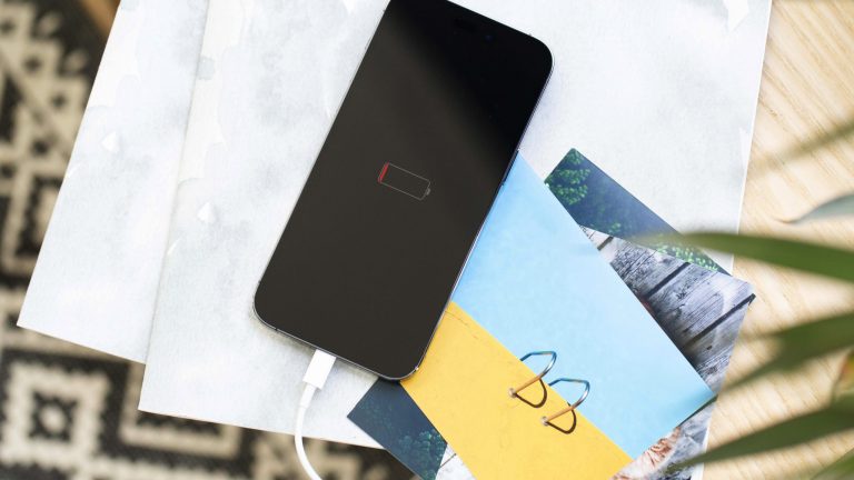 Ein leeres iPhone liegt auf einigen Zetteln und Postkarten. Auf dem Display ist eine leere Batterie zu sehen.