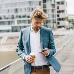 Eine Person mit Kaffeebecher in der Hand spaziert und schaut dabei auf ihr Smartphone.