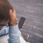 Eine Person sitzt drau&szlig;en mit einem Smartphone in der Hand, dessen Display gebrochen ist.