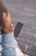 Eine Person sitzt draußen mit einem Smartphone in der Hand, dessen Display gebrochen ist.