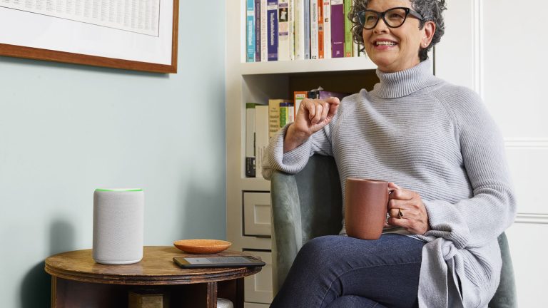 Eine Person sitzt an einem Kaffeetisch, auf dem ein smarter Lautsprecher steht.