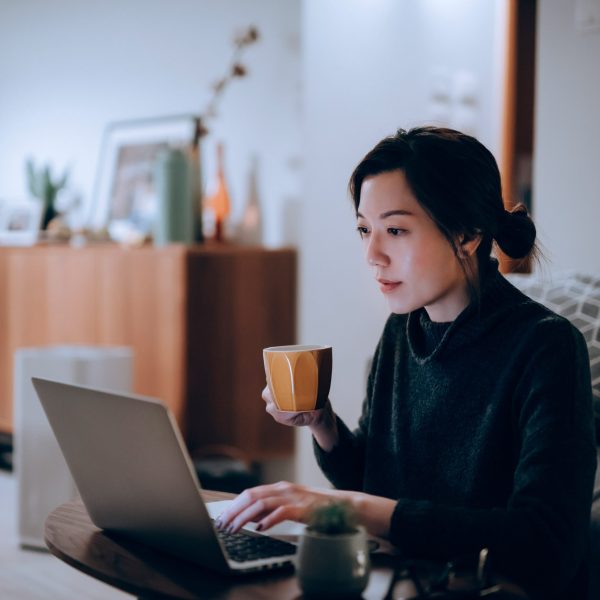 Eine Person mit einer Kaffeetasse in der Hand sitzt vor einem Laptop.