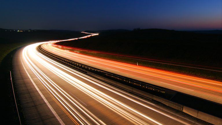 Blick auf eine Autobahn, auf der die Lichter der Autos dank Langzeitbelichtung zu Streifen verschwimmen.