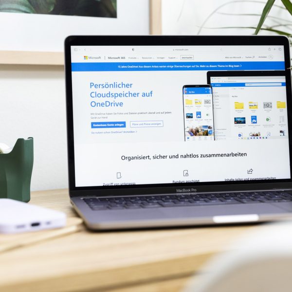 Ein MacBook Pro mit ge&ouml;ffneter OneDrive-Produktseite steht auf einem Tisch.