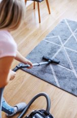 Eine Person saugt mit einem Staubsauger über einen Teppich.