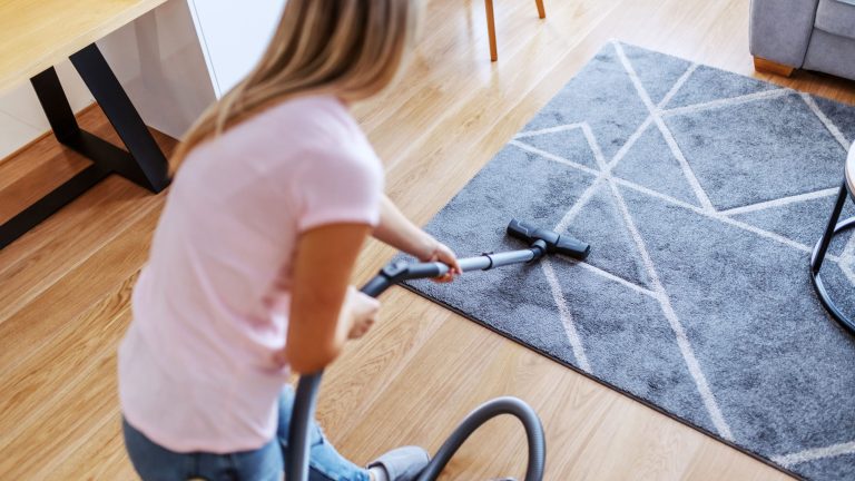 Eine Person saugt mit einem Staubsauger über einen Teppich.