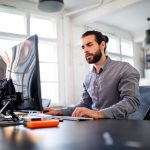 Eine Person sitzt vor einem Rechner in einem B&uuml;ro.