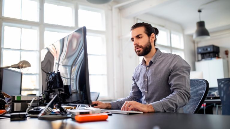 Eine Person sitzt vor einem Rechner in einem Büro.