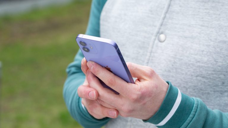 Eine Person steht vor einer Grünfläche und hält ein iPhone in ihren Händen.