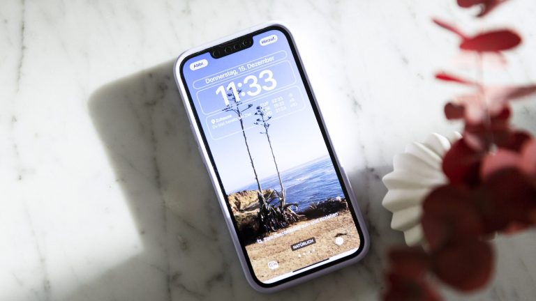 Ein iPhone mit eingeschaltetem Display liegt auf einem Marmortisch. Auf dem Bildschirm ist der neue Sperrbildschirm zu sehen, der sich seit iOS 16 stärker individualisieren lässt.