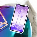 Ein iPhone liegt mit eingeschaltetem Bildschirm in einer Schale. Auf dem Ger&auml;t ist ein lilafarbenes Hintergrundbild zu erkennen.