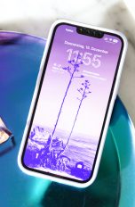 Ein iPhone liegt mit eingeschaltetem Bildschirm in einer Schale. Auf dem Gerät ist ein lilafarbenes Hintergrundbild zu erkennen.