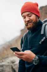 Eine in Wandergarderobe gekleidete Person in den Bergen schaut auf ein Smartphone.
