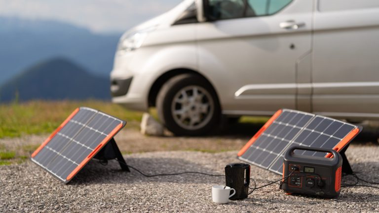 Vor einem Multivan stehen zwei Solarpanels, eine Powerstation, ein Wasserkocher und eine Tasse.