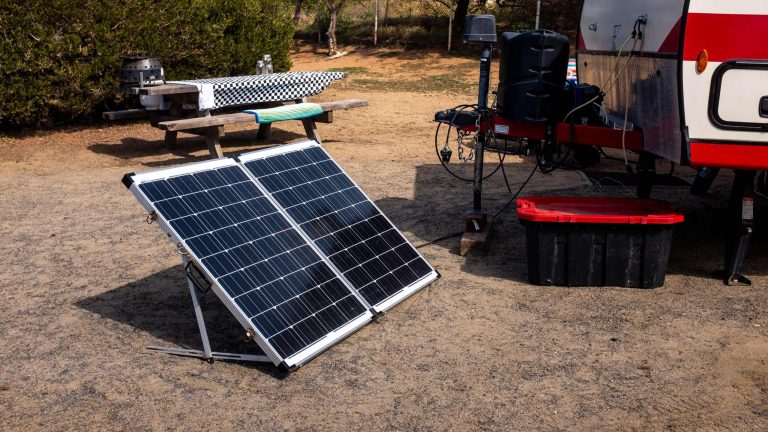 Vor einem Wohnwagen steht eine mobile Powerstation mit einem Solarpanel.