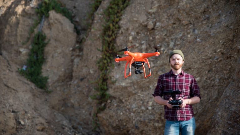 Vor einem Felsen steht eine Person, die eine Drohne fliegen lässt.