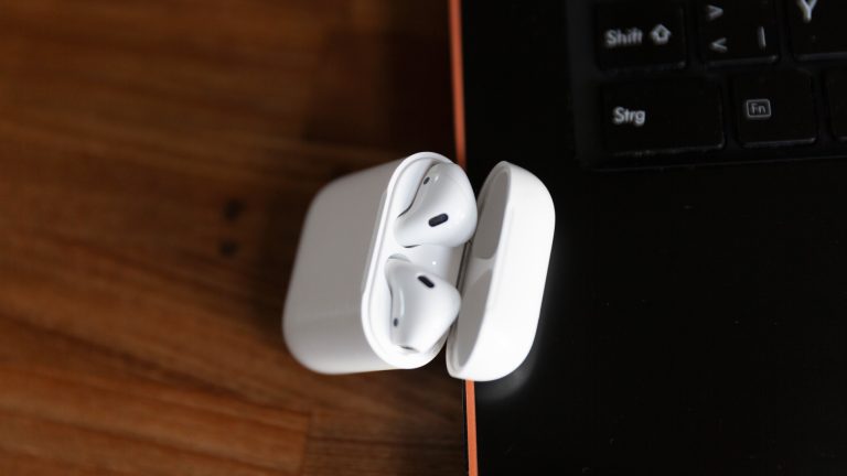 AirPods in ihrem Case liegen neben einem Windows-Laptop.