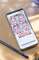 Ein Android liegt auf einem Holztisch. Auf dem Display ist ein Screenshot der App „YouCam Makeup“ zu sehen.