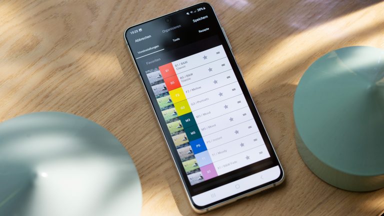 Ein Android-Gerät liegt mitsamt Dekorationselementen auf einem Tisch. Auf dem Bildschirm ist ein Screenshot der App “VSCO: Foto- und Video-Editor“ zu sehen.