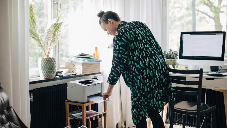 Eine Person steht vor einem Drucker und nimmt einen Ausdruck heraus.
