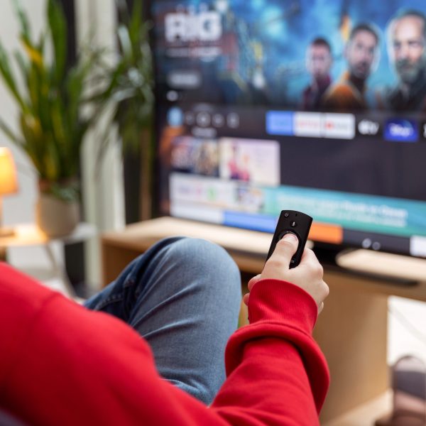 Eine Person sitzt vor einem Fernseher mit der Fernbedienung eines Fire-TV-Sticks in der Hand.