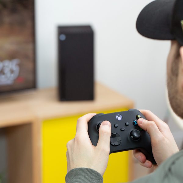 Eine Person sitzt vor einem Fernseher und spielt mit einem Controller in der Hand auf einer Xbox Series X.