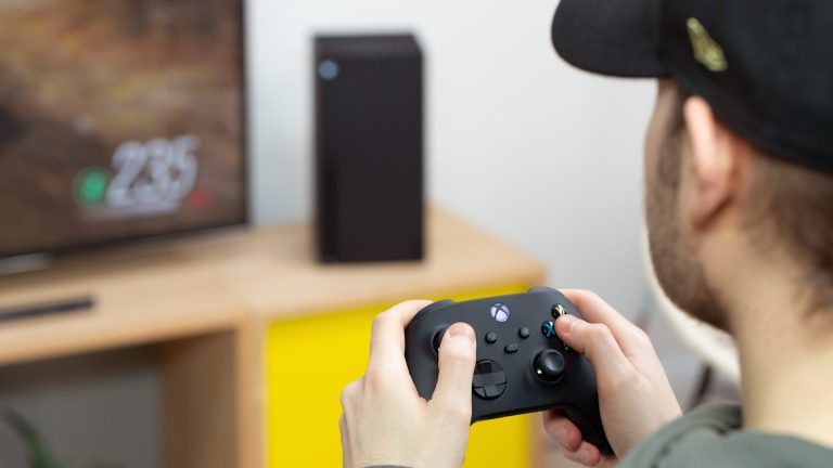 Eine Person sitzt vor einem Fernseher und spielt mit einem Controller in der Hand auf einer Xbox Series X.