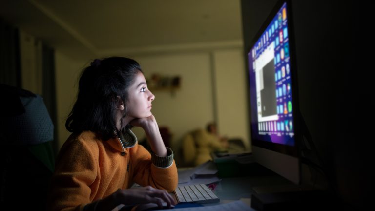 Eine Person sitzt vor einem Rechner in einem dunklen Raum.