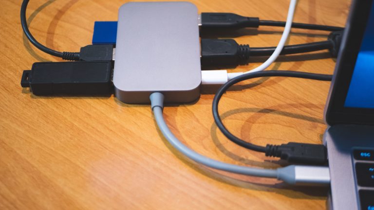 Eine kabelgebundene Dockingstation hängt an einem Laptop. In die Dockingstation eingesteckt sind mehrere Kabel und ein USB-Adapter.